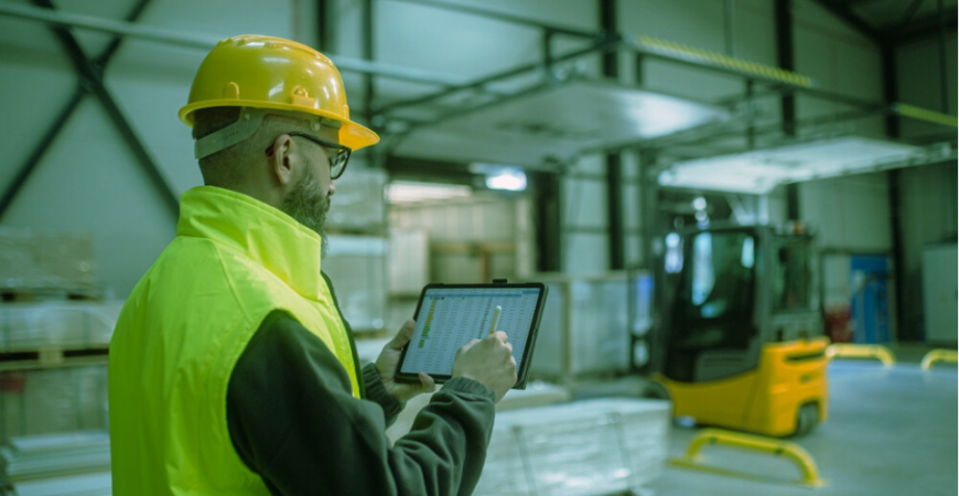 Shipping manager working though retail logistics, holding a tablet with spreadsheet inside warehouse
