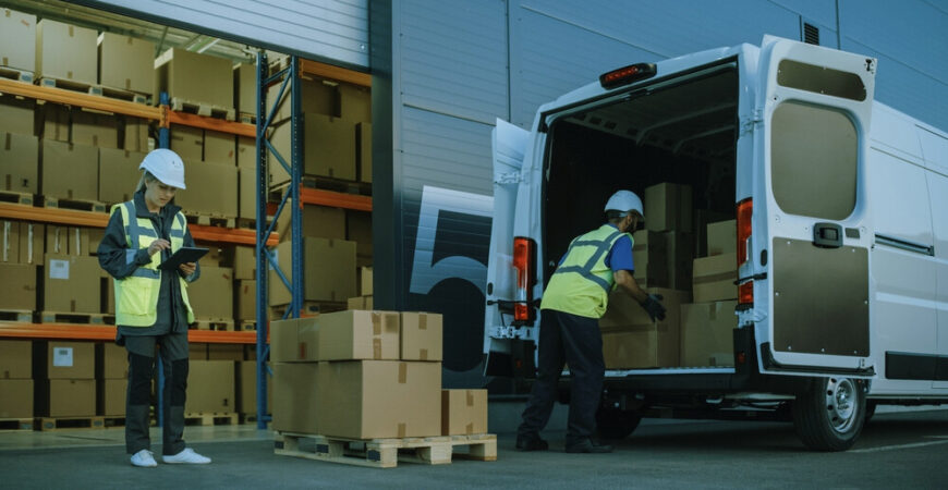 Outside of Logistics Distributions Warehouse With Inventory Manager Using Tablet Computer, talking to Worker Loading Delivery Truck with Cardboard Boxes. Online Orders, Purchases, E-Commerce Goods