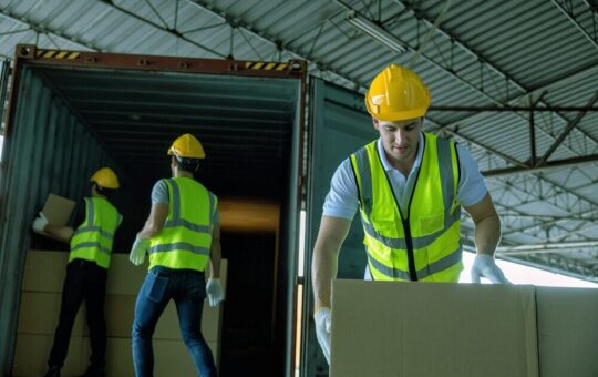 3 Workers hand carry carton box take from 40 feet steel container one by one and stack on floor